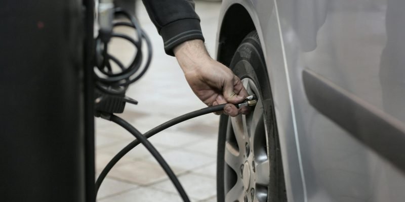 Mechanic inflating a car tire inside an auto repair shop, ensuring optimal tire pressure.